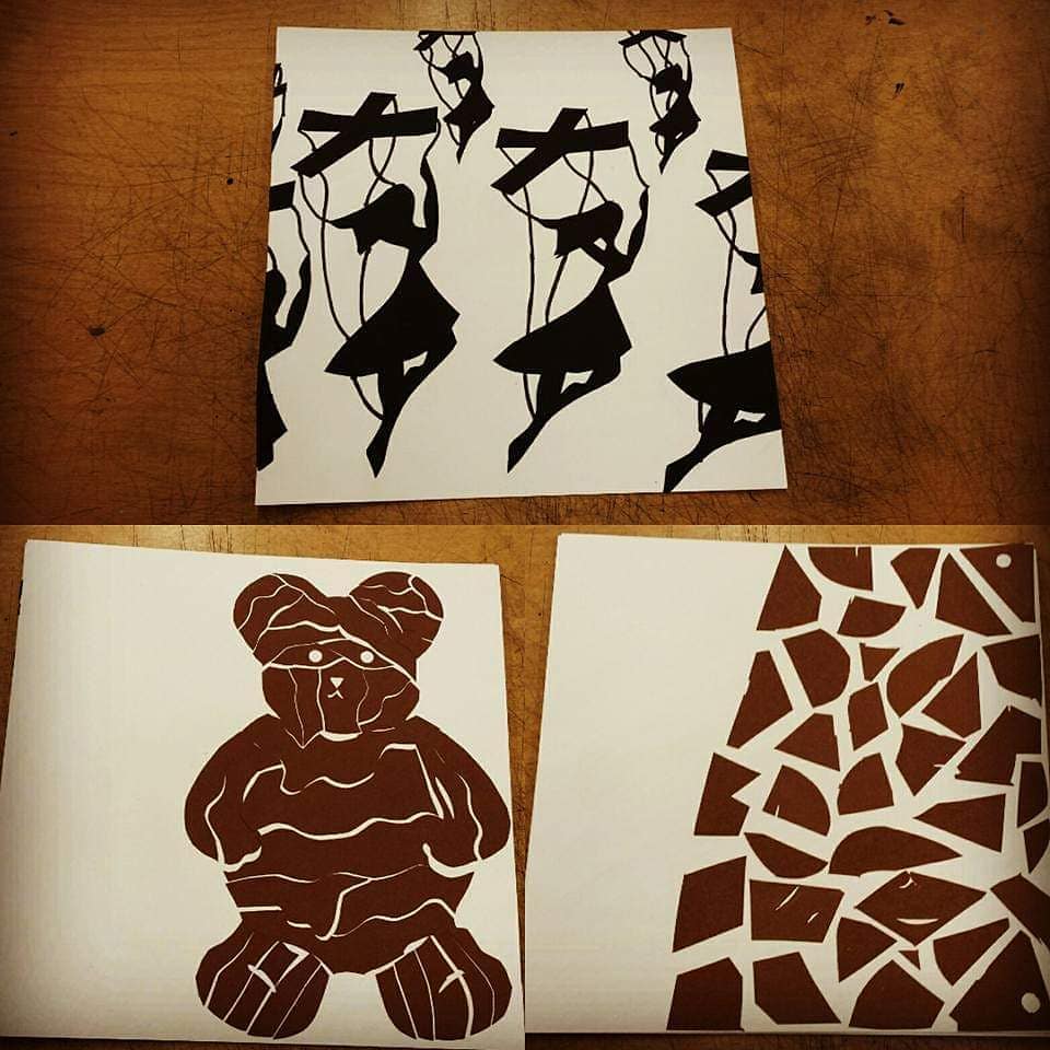 3 art pieces. 1 marionettes dance in a circle motion. 2nd is a bear cut into a puzzle. 3 is an abstract piece with brown puzzle pieces scattered to 2/3 of the right side of the page.